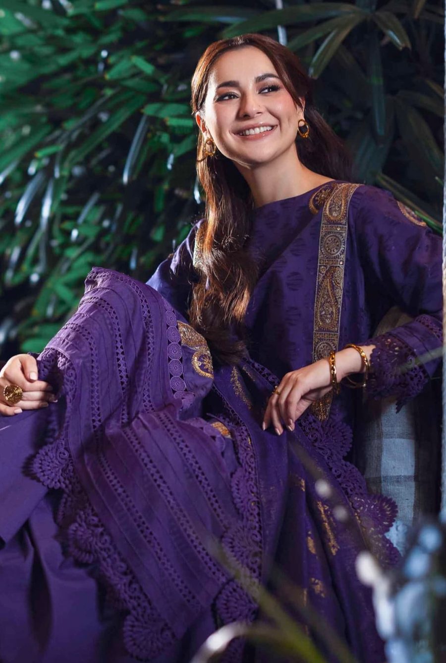 Model in purple wearing gold hoops, bangles and a statement ring