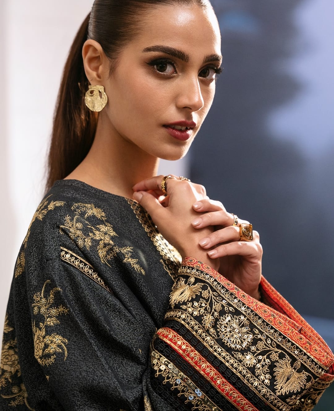 Model wearing gold statement earrings and stacked signet rings